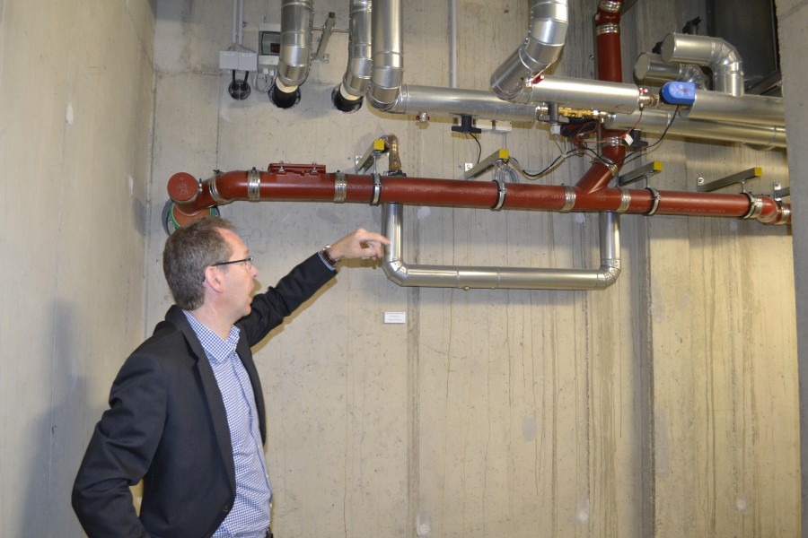 Martin Heuser von der Mainova zeigt, wo die Wärme aus den Plusenergiehäusern in die Heizzentrale und damit in das Nahwärmenetz der Parkstadt abgegeben wird. Quelle: AEE